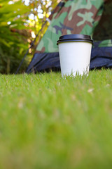 hot coffee drink, white disposable cup on green grass lawn campsite