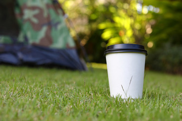 hot coffee drink, white disposable cup on green grass lawn campsite