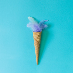 Ice cream cone and purple feathers of a bird on pastel blue background. Flat lay. Minimal  concept.
