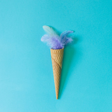 Ice cream cone and purple feathers of a bird on pastel blue background. Flat lay. Minimal  concept.