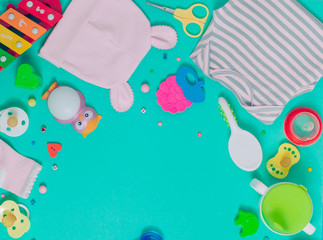 Baby clothes, soother, spoon, brush and toys over green background