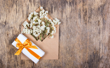 White dried flowers in a paper envelope and a box with a gift with a golden ribbon. Copy space