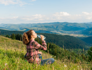 young woman drinking water in the mountains top