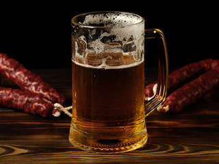 Spreading pint of light beer and sausage on a wooden table.