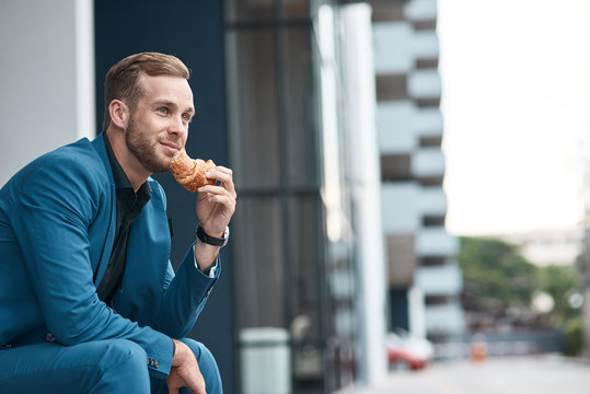 Positive Hungry Businessman Eating A Croissant