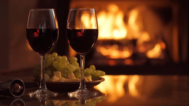 Two red wine wineglasses over fireplace background.