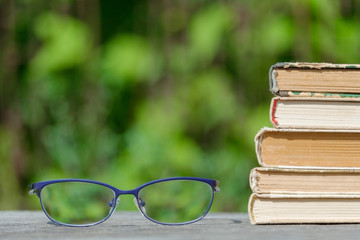 a stack of books and glasses lie on a wooden table on a background of nature