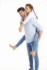 Happy young couple having fun against white background. Man giving piggy back to her girlfriend.