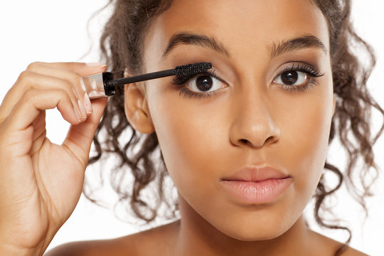 a young dark skinned woman applying a mascara to her eyelashes