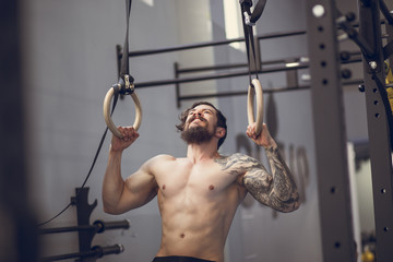 Muscle-up exercise young man doing intense cross fit workout at the gym on gymnastic rings