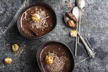 A cozy autumn delicate dessert made of chocolate mousse, chocolate chips and caramel popcorn in porcelain dark bowls on a simple gray stone background. Top View.