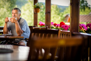 Handsome senior man enjoying his morning coffee on a mountain hotel terrace, while on vacation