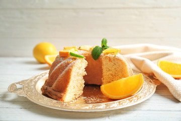 Tray with delicious sliced cake and citrus fruits on wooden table