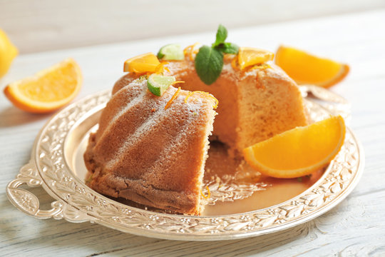 Tray with delicious sliced cake and citrus fruits on wooden table
