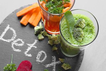 Fresh juices in glasses and ingredients on slate plate with word DETOX
