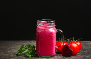 Mason jar with fresh vegetable juice and ingredients on table against black background