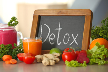 Small chalkboard with word DETOX, fresh juices and ingredients on table
