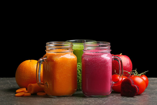 Mason jars with fresh juices and ingredients on table against black background
