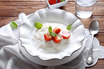 Creamy rice pudding with strawberry in plate on wooden table