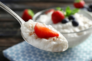 Spoon with creamy rice pudding and strawberry on blurred background
