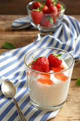 Creamy rice pudding with strawberry in glass on wooden table