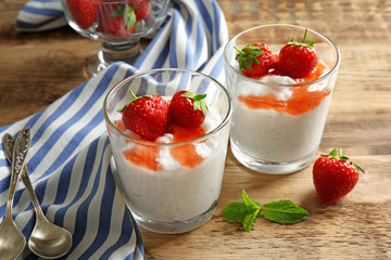 Creamy rice pudding with strawberry in glasses on wooden table