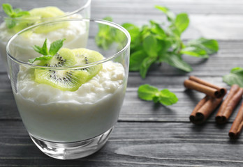 Creamy rice pudding with kiwi in glass on wooden table