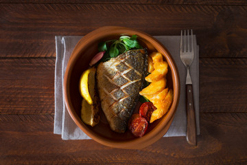 Baked dorado with fresh salad and vegetables. Top view. Brown wooden table