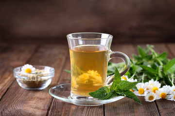 Cup of herbal tea and chamomile flowers on wooden table