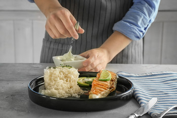 Woman pouring sauce onto plate with delicious salmon and rice in kitchen