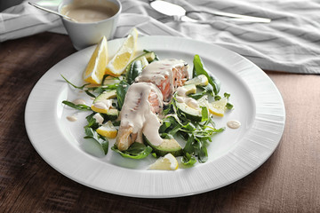 Plate with slice of salmon, herbs and delicious sauce on wooden table