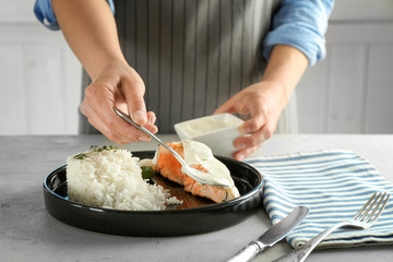 Woman pouring sauce onto plate with delicious salmon and rice in kitchen