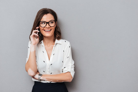 Happy woman in eyeglasses and business clothes talking by smartphone