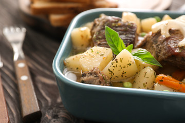 Blue casserole with tasty meat and potatoes on table, close up