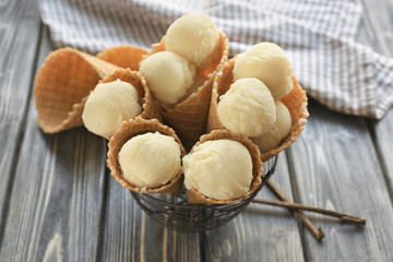 Metal basket with delicious waffle cones of vanilla ice-cream on table