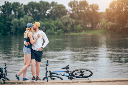 Couple in love resting on a boardwalk with a bike at the lake