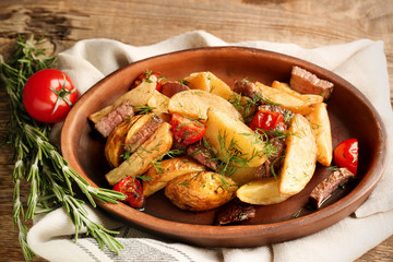 Wooden plate with delicious baked potato wedges on table