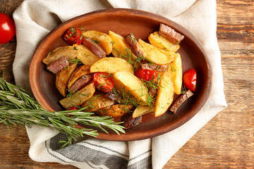 Wooden plate with delicious baked potato wedges on table