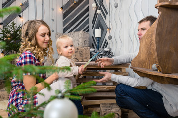 Portrait of young family: mom, dad and little son. All of them sitting in decorated room, child holding the children book. Concept of Merry Christmas and New Year