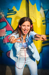 Fototapeta na wymiar Beautiful woman listening to music on red headphones sings and dances on graffiti background. shows thumbs up 