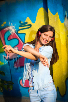 Beautiful woman listening to music on red headphones and dances on graffiti background 
