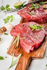 Fresh raw meat. Beef tenderloin, steaks, on a white marble table. With olive oil, spices for cooking - basil, rosemary, coriander, parsley, garlic, lemon, salt, pepper. Copy space