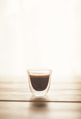 A single shot of espresso in a double wall glass on a wooden table. Side view.