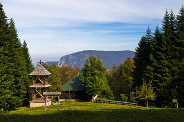 Fototapeta na wymiar Viewpoint on a landscape of mount Bobija, meadow in front of an old wooden church surrounded by tall fir trees with rocky peaks in backgound, west Serbia