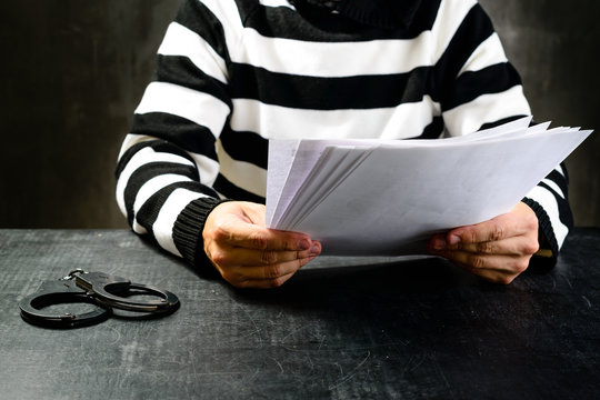 unidentified prisoner in prison stripped uniform sitting on the chair in the dark interrogation room and reading official papers. The interrogation of the arrested