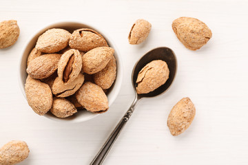 Almond in shell in a white ceramic bowl with metal spoon near, top view, flat lay