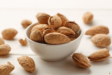 Heap of almond in shell in a white bowl on a wooden table