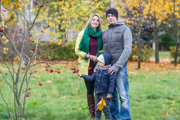 Happy family of three standing together in the garden in autumn