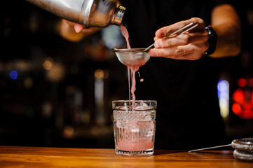 Fototapeta na wymiar Bartender hand pouring pink cocktail drink in bar