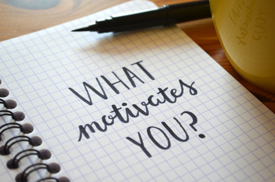 “WHAT MOTIVATES YOU?” written in notebook on desk with cup of coffee